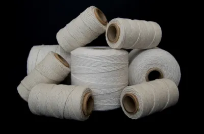 Several spools of white twine are arranged in a pile against a black background.