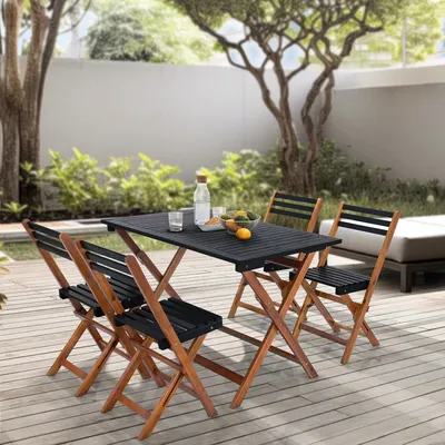 An outdoor patio scene with a wooden table and chairs set up on a wooden deck, surrounded by greenery and a wall.