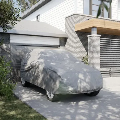 A car covered with a grey car cover parked in front of a modern house and garage.