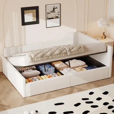 A white upholstered daybed with storage drawers underneath, filled with folded clothes and storage bins. The bed is made with a beige quilted comforter.