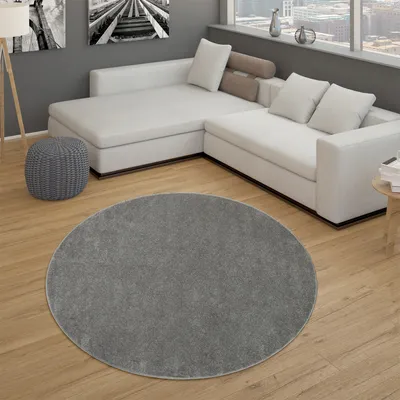 A round, dark gray rug is placed on a wooden floor in a modern living room with a white sectional sofa.
