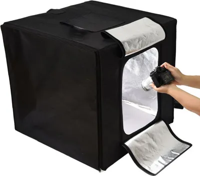 A black photography light tent with silver interior, being used by a person holding a camera.
