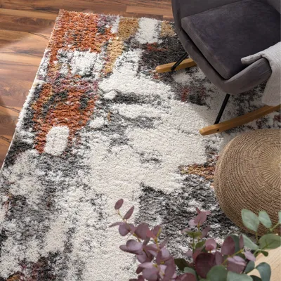 A close-up view of a shaggy rug with an abstract design, placed on a wooden floor next to a rocking chair and a woven pouf.
