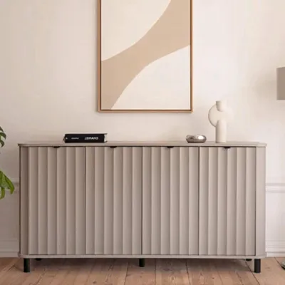 A modern gray sideboard with fluted doors is displayed in a room with artwork on the wall and a lamp in the background.