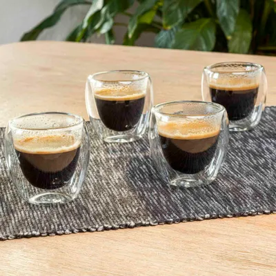 Four double-walled espresso cups filled with dark espresso sit on a textured mat on a wooden table.
