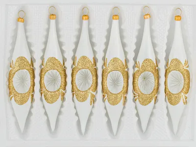 Six white and gold glass icicle ornaments arranged in a white box.
