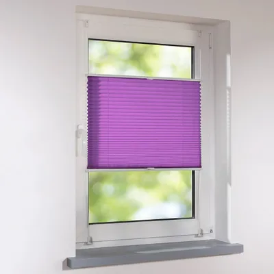 A purple pleated blind is installed in a white window frame, with a blurred green background visible through the window.