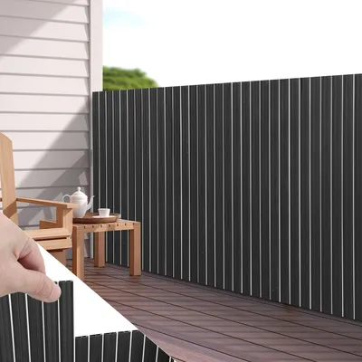 A balcony with a wooden deck, a chair, a table with tea set, and a dark gray privacy screen.