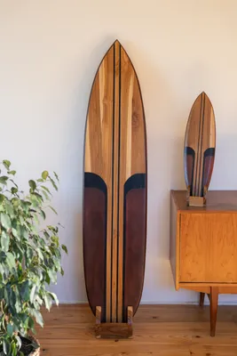 Two wooden surfboards are displayed in a room with a plant and a cabinet.