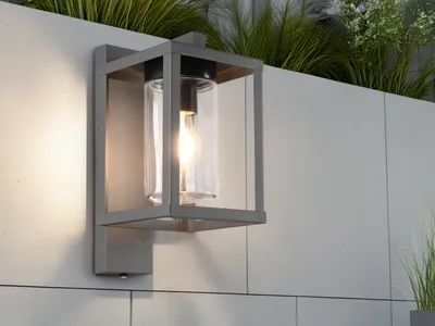 An outdoor wall lamp is mounted on a tiled wall, with plants in the background.