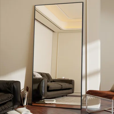 A full-length mirror is placed in a living room setting, reflecting a sofa and part of the room's interior.