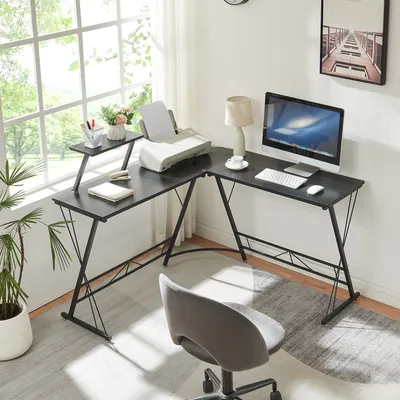 A home office setup with an L-shaped desk, computer, printer, and chair, near a large window.