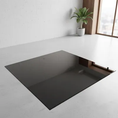 A black glass hearth plate is placed on a concrete floor in a room with a white wall and a window.