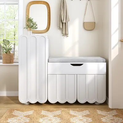 A white shoe cabinet with a gray cushion and a small beige handbag hanging on a hook above it, placed in a hallway with a rug on the floor.