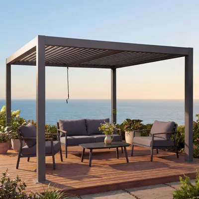 A pergola with outdoor furniture set up on a wooden deck overlooking the ocean.
