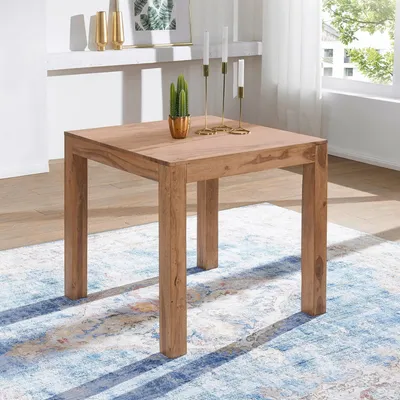 A wooden dining table with a cactus and candles on top, placed on a patterned rug in a well-lit room.