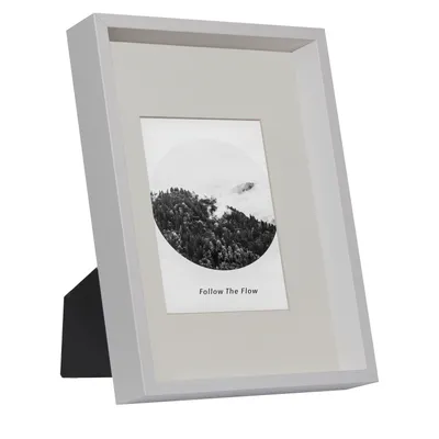 A white picture frame with a black stand, displaying a black and white photograph of a forest.