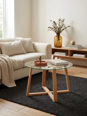 Couchtisch aus Eiche mit Glasplatte in einem modernen Wohnzimmer neben einem Sofa. Der runde Sofatisch (58x47cm) steht auf einem dunklen Teppich und schafft eine warme Atmosphäre._#sku_SAFWL6.494#