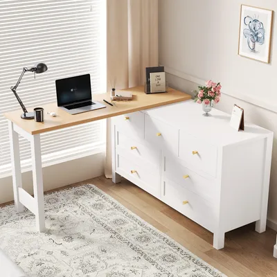 A white dresser with a wooden desk extension, set up as a home office, next to a window with blinds.