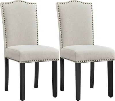 Two beige upholstered dining chairs with black legs and nailhead trim, presented against a white background.