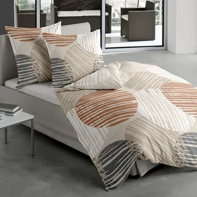 A bed with a patterned duvet and pillows in a modern room with large windows.