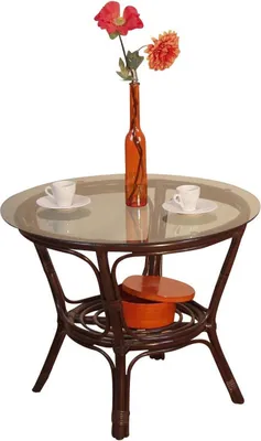 A round rattan table with a glass top, decorated with a vase of flowers and two coffee cups.