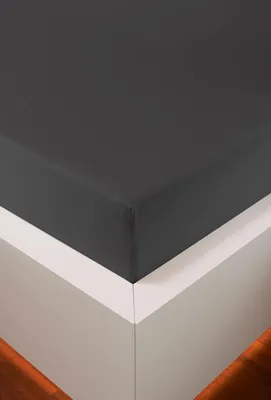 A close-up view of a dark gray fitted sheet on a white bed frame.