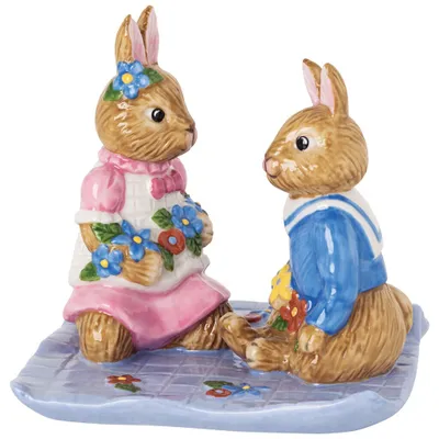 Two ceramic bunnies sitting on a blue checkered mat with flowers.