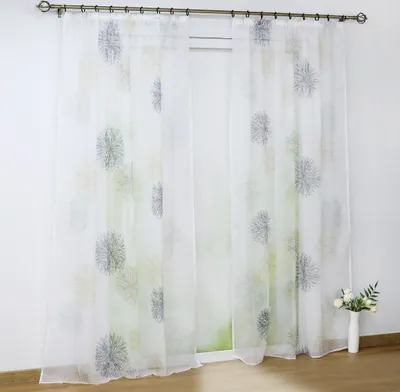 Two sheer curtains with a dandelion-like print hanging on a curtain rod in front of a window.