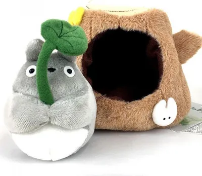 A plush toy of Totoro sitting next to a tree stump.