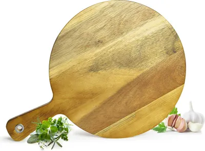 A round wooden cutting board with a handle, placed on a white background with some herbs and garlic.