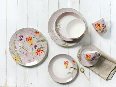 A collection of floral-patterned tableware is arranged on a white wooden surface.