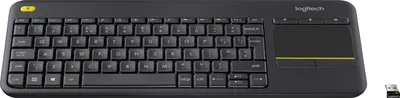 A black Logitech K400 Plus keyboard with a built-in trackpad is shown from a slightly elevated front-facing angle against a white background. A small USB receiver is visible in the bottom right corner.