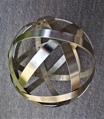 A metallic sphere made of interwoven bands sits on a textured gray surface.