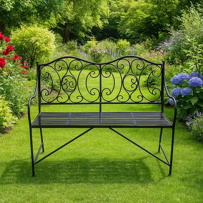 A black metal garden bench sits on a lush green lawn in a garden setting with flowers and trees.