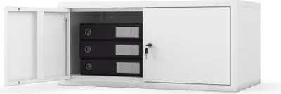 A white metal filing cabinet with its left door open, revealing three black binders inside. The right door is closed and has a key lock.