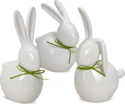 Three white ceramic Easter bunnies with green ribbon bows against a white background.