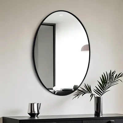 A modern interior scene featuring an oval mirror on a wall above a dark dresser.