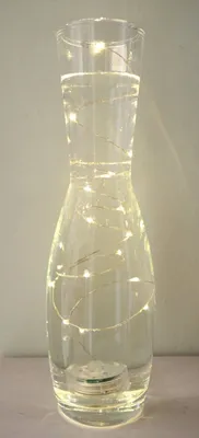 A clear glass vase filled with water and illuminated by a string of LED lights.