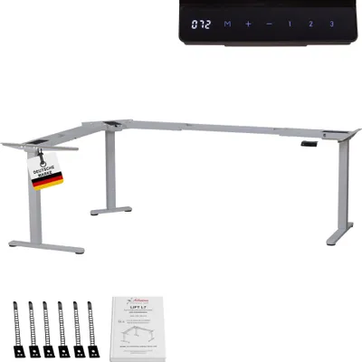 A silver L-shaped standing desk frame with a control panel and accessories laid out below.
