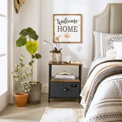 A bedroom scene with a nightstand next to a bed, decorated with plants and wall art.