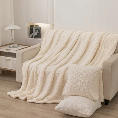 A cream-colored sherpa blanket is draped over a sofa, with two matching pillows in the foreground.