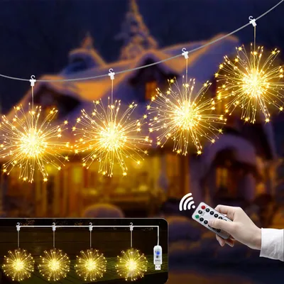 A hand holding a remote control is shown in the foreground, with a string of starburst-shaped LED lights hanging in the midground against a blurred background of a snowy house.