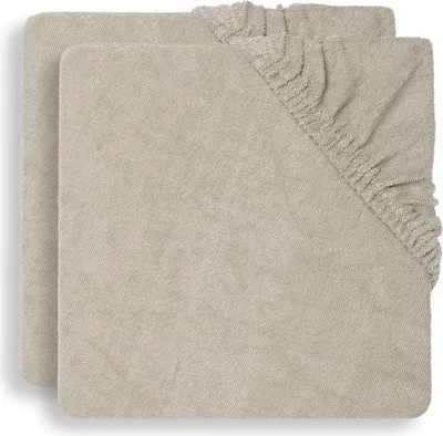 Two beige fitted sheets are stacked on top of each other, with the top sheet showing its elasticized corner.