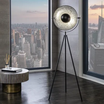 A modern living room with a city view, featuring a tripod floor lamp and a side table.