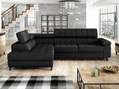 A modern living room with a black sectional sofa, a staircase, bookshelves, and a coffee table.