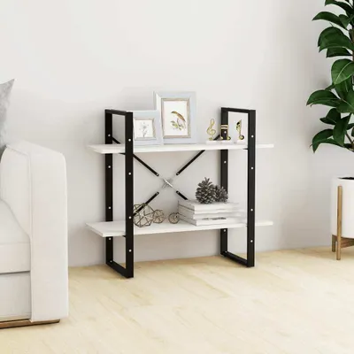 A white bookshelf with two shelves is placed against a white wall, next to a white sofa. The shelves are decorated with picture frames, decorative items, and books. A large green plant in a white pot is visible on the right side of the image.