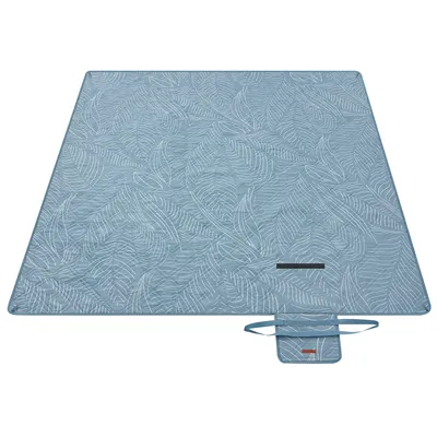 A light blue picnic blanket with a white tropical fern pattern is laid out flat on a white background. A small folded pouch with handles is attached to the blanket.