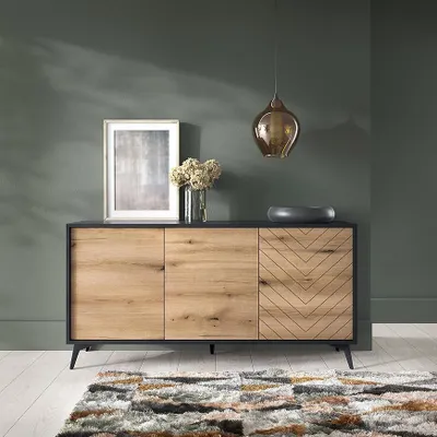 A modern sideboard with a wooden front and black frame, placed in a room with dark green walls and a patterned rug.