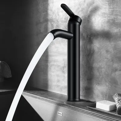A black matte faucet with water flowing out, set against a textured gray wall and a countertop.